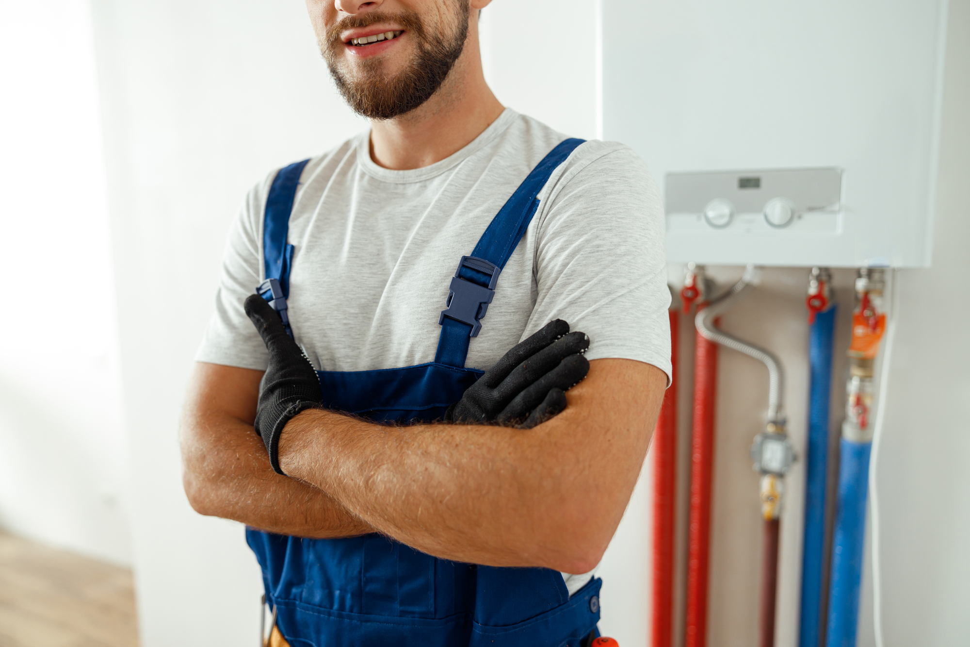 Cropped shot of smiling technician installing and setting the new gas boiler for hot water and heating, standing with arms crossed. Manual work, maintenance concept
